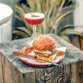 木のテーブルに並ぶバナナママのスマッシュバーガーとカクテル